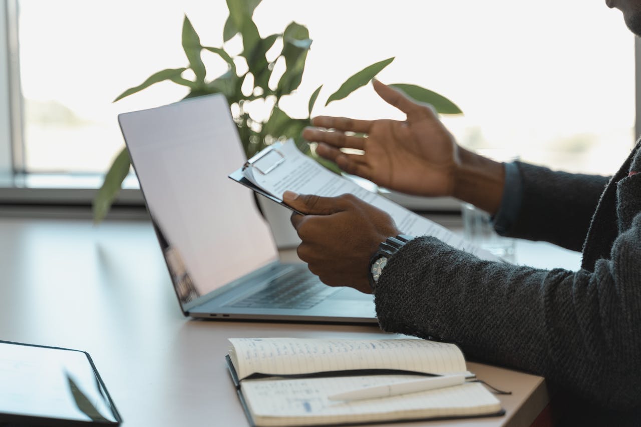 Business professional reviewing documents at a workspace with laptop and notebook.